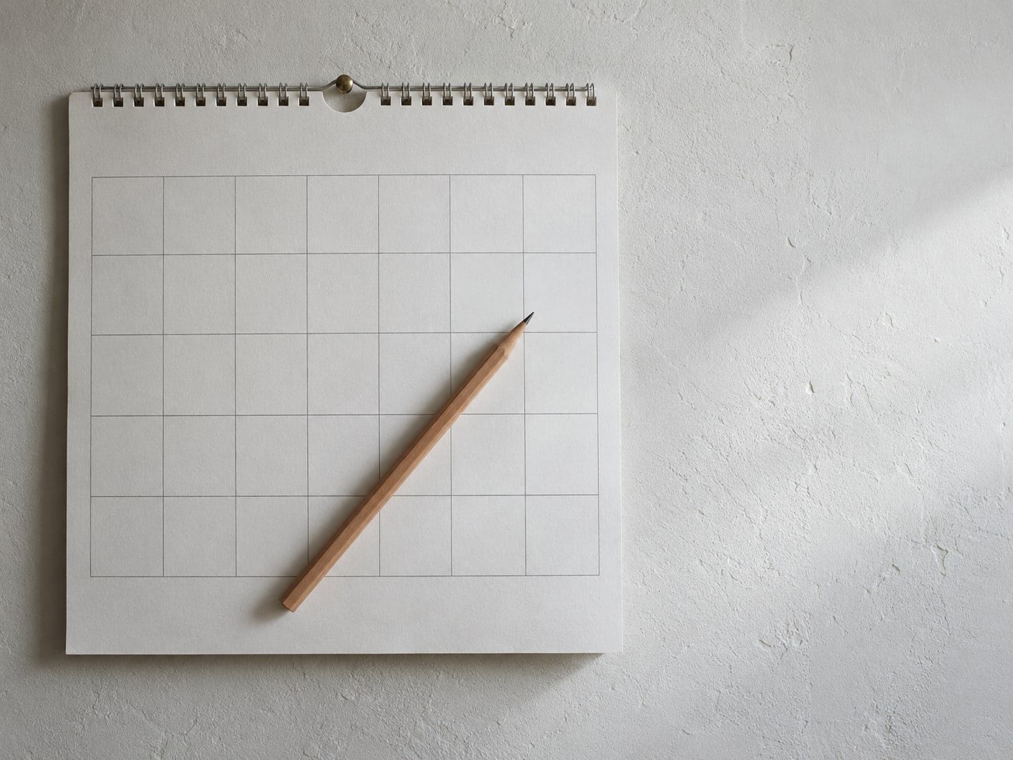 Un calendario de pared con varias fechas en blanco y un lápiz atravesado encima.