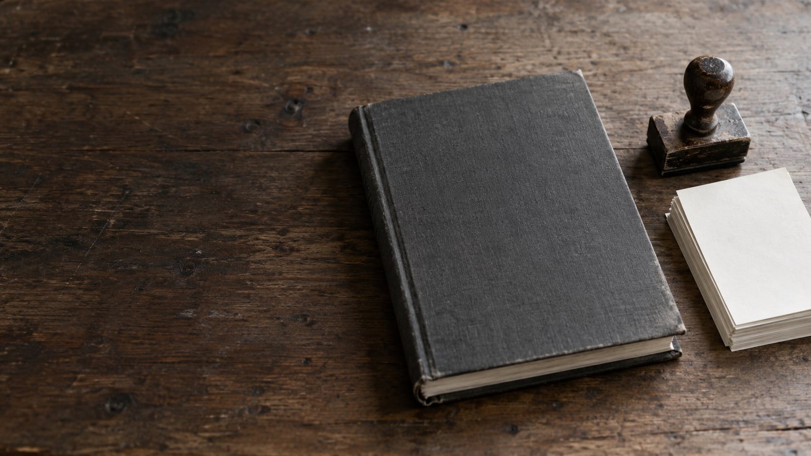 Un libro de contabilidad cerrado y un sello de goma sobre un escritorio de madera gastada, junto a una pequeña pila de órdenes de trabajo en papel.