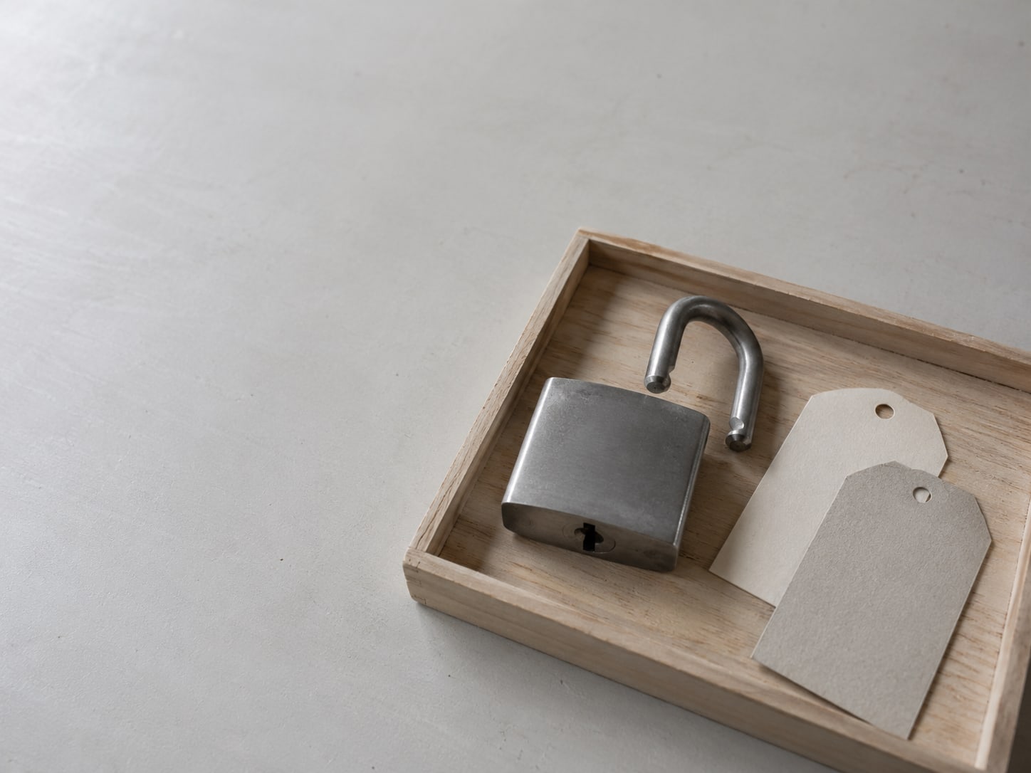 A padlock rests open on a small wooden tray beside two unmarked paper tags in different colors.