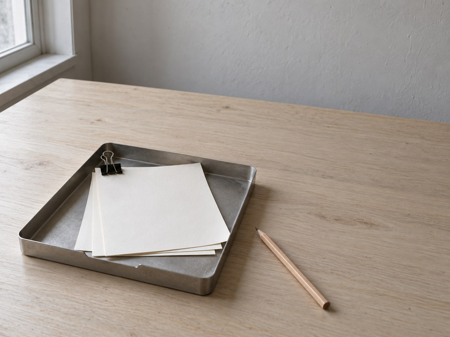 A small tray holding three paper sheets fastened with a binder clip, a pencil laid beside it on a clean desk.