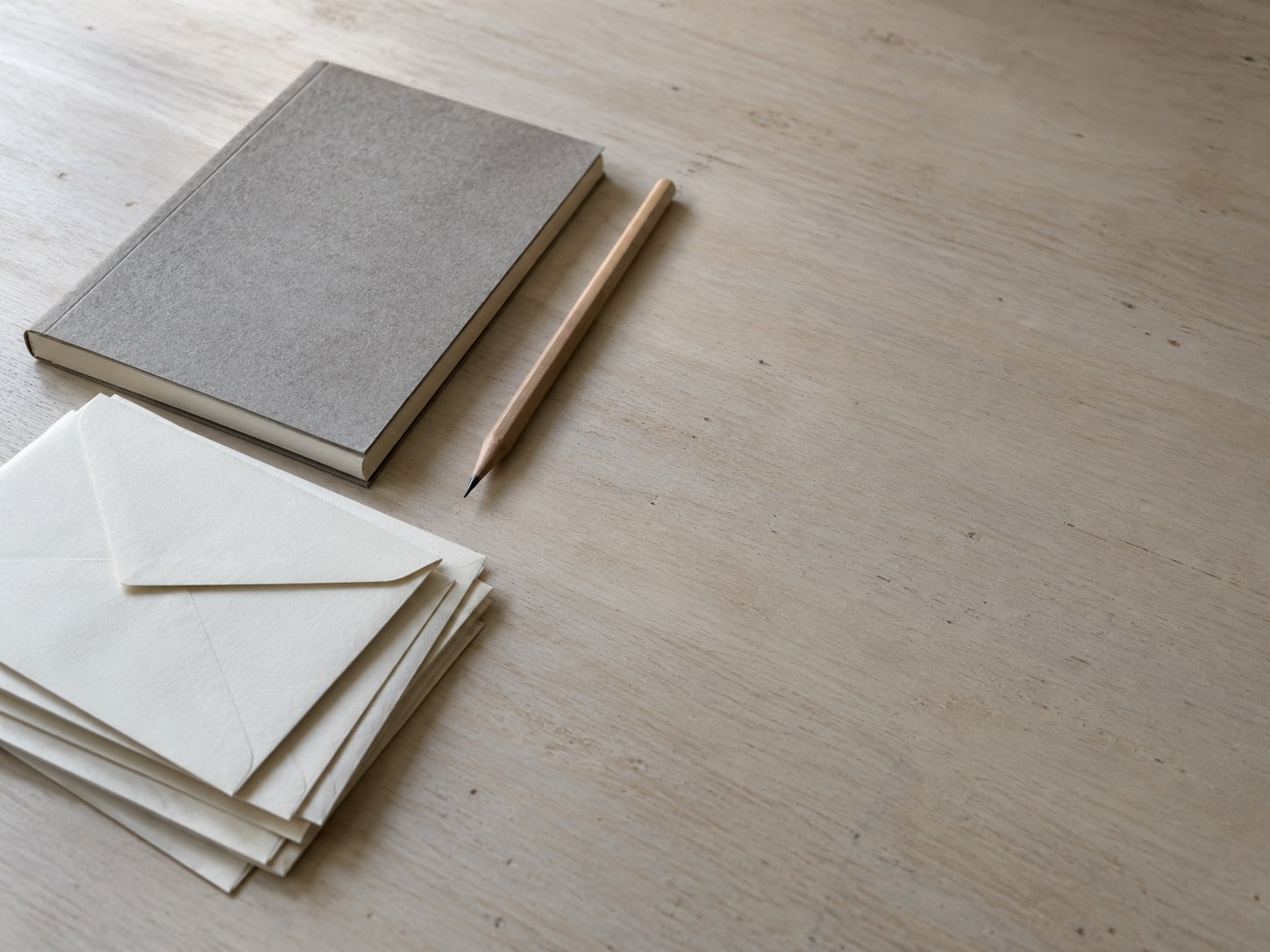 Several sealed blank paper envelopes stacked beside a plain notebook and a pencil on a clean desk.