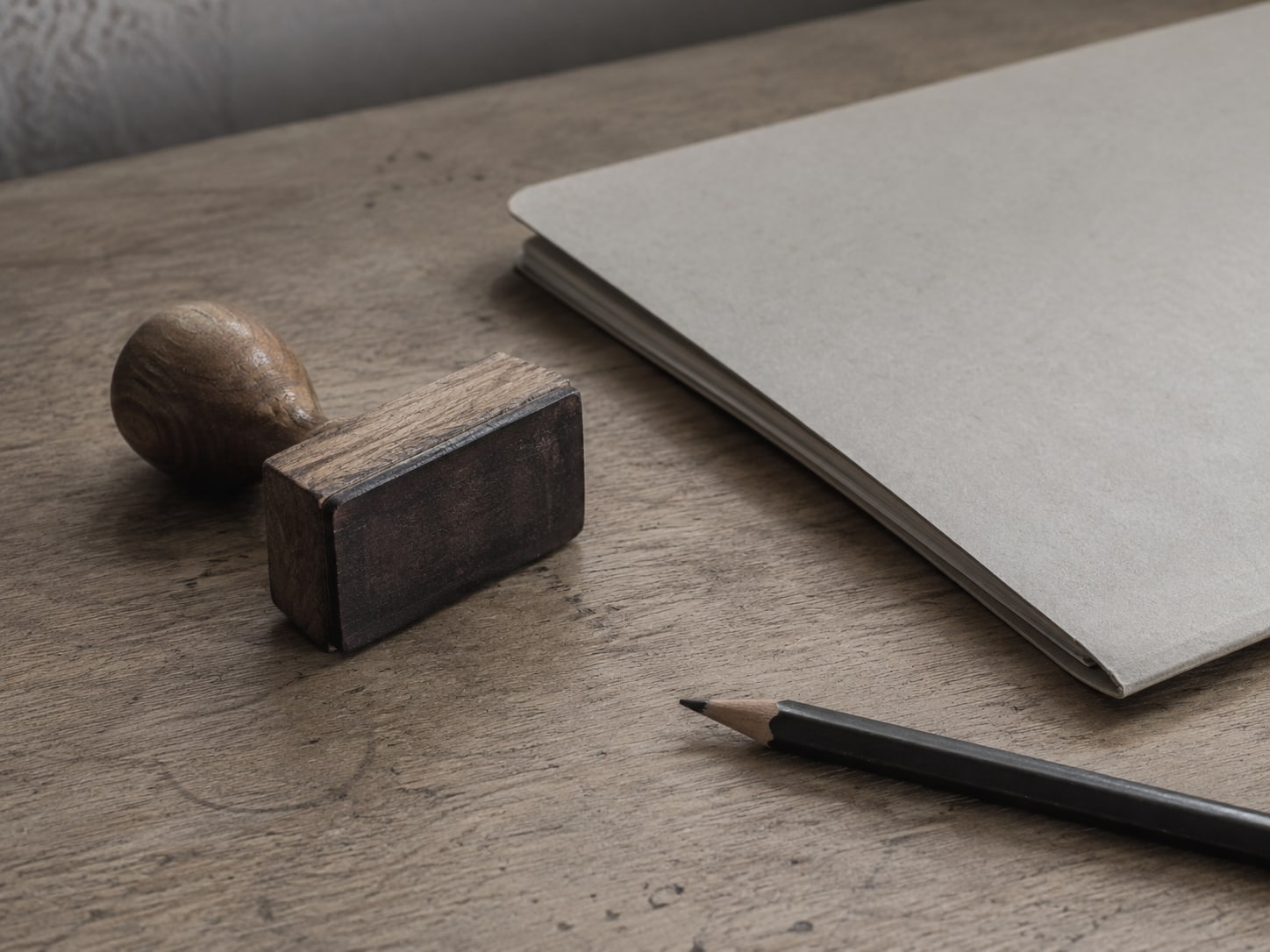 A rubber stamp resting beside a closed folder and a pencil on a plain desk.