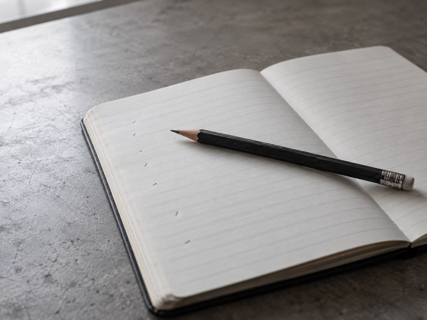 Un lápiz sobre un cuaderno abierto cuyas líneas tienen unas pocas marcas tenues e ilegibles.