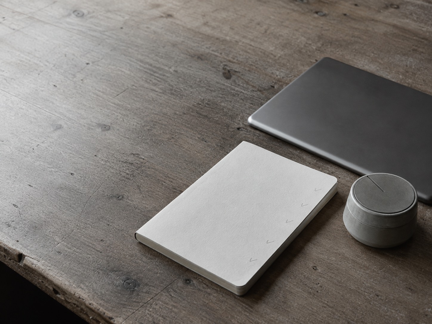 A notebook open to a page of faint pencil marks beside a closed laptop and a cup of coffee on a wooden desk.