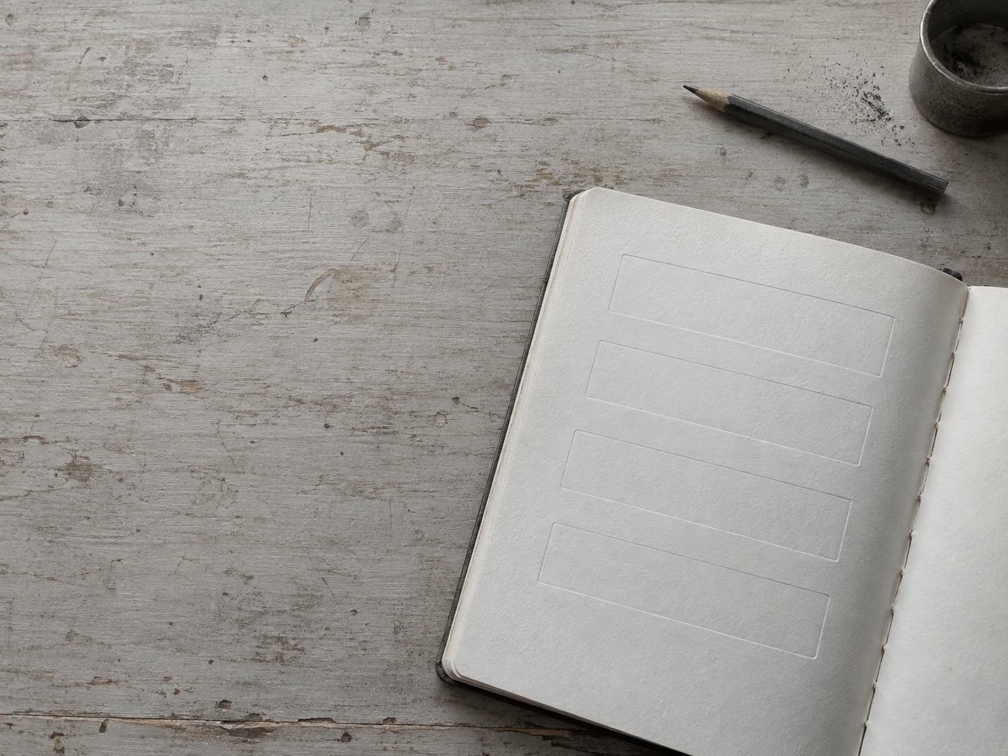 Una libreta abierta con cuatro recuadros tenues trazados en la página y un lápiz cerca.
