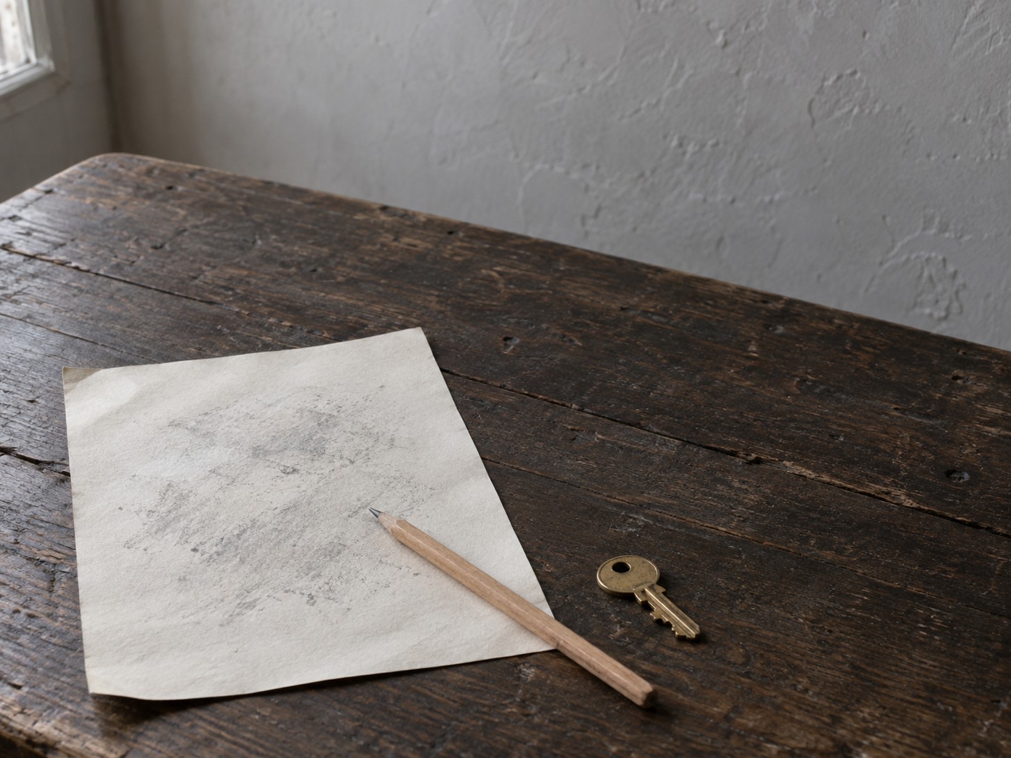 Una sola hoja de papel con marcas de lápiz tenues e ilegibles, un lápiz y una pequeña llave de latón sobre una mesa de madera oscura.