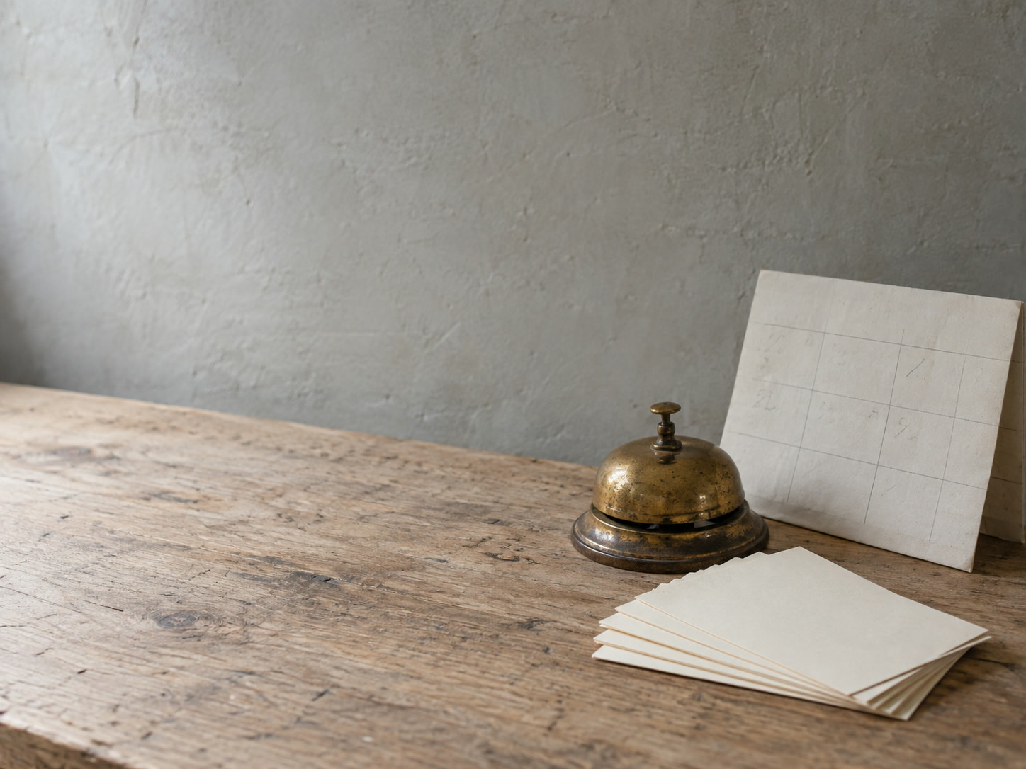 A set of blank index cards fanned out beside a brass desk bell and a folded paper calendar with faint unreadable pencil marks.