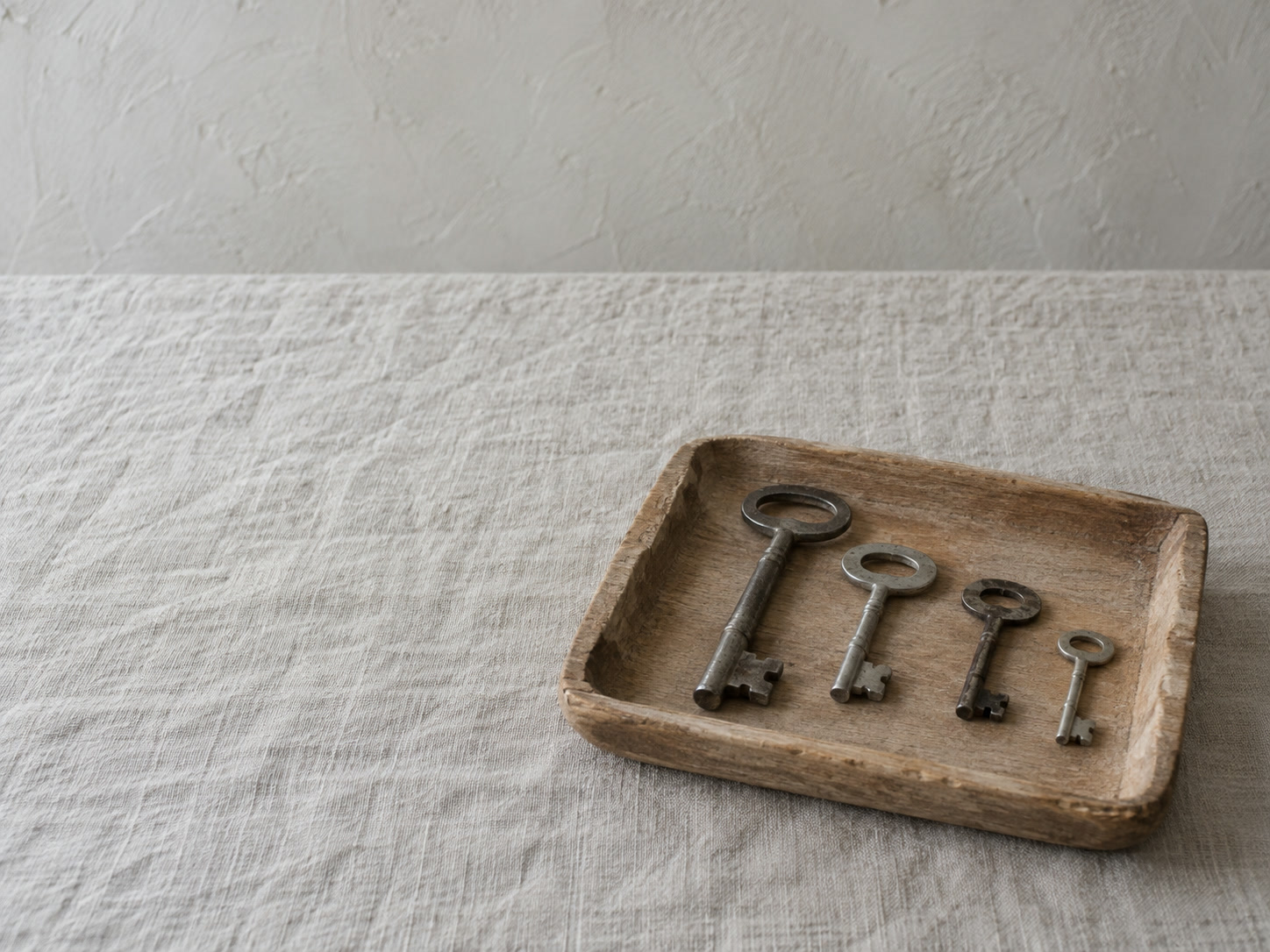 A small wooden tray holding four plain unmarked keys of different sizes on a light linen tablecloth.