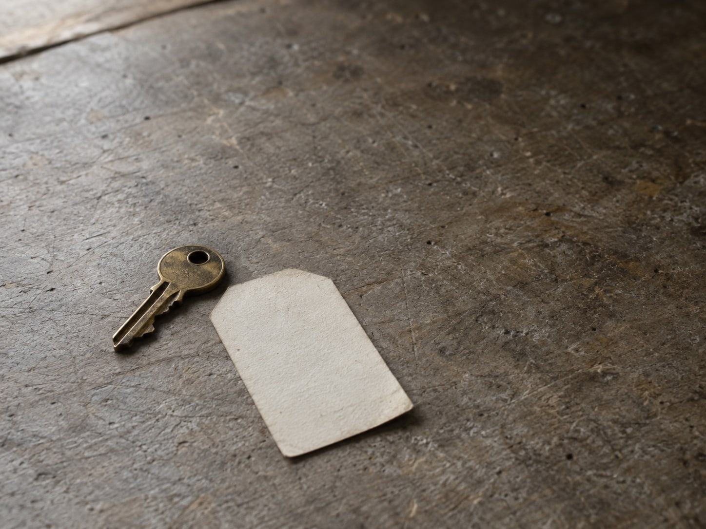 Una pequeña llave de latón y una etiqueta de papel en blanco sobre un mostrador desgastado, junto a una agenda de citas cerrada.