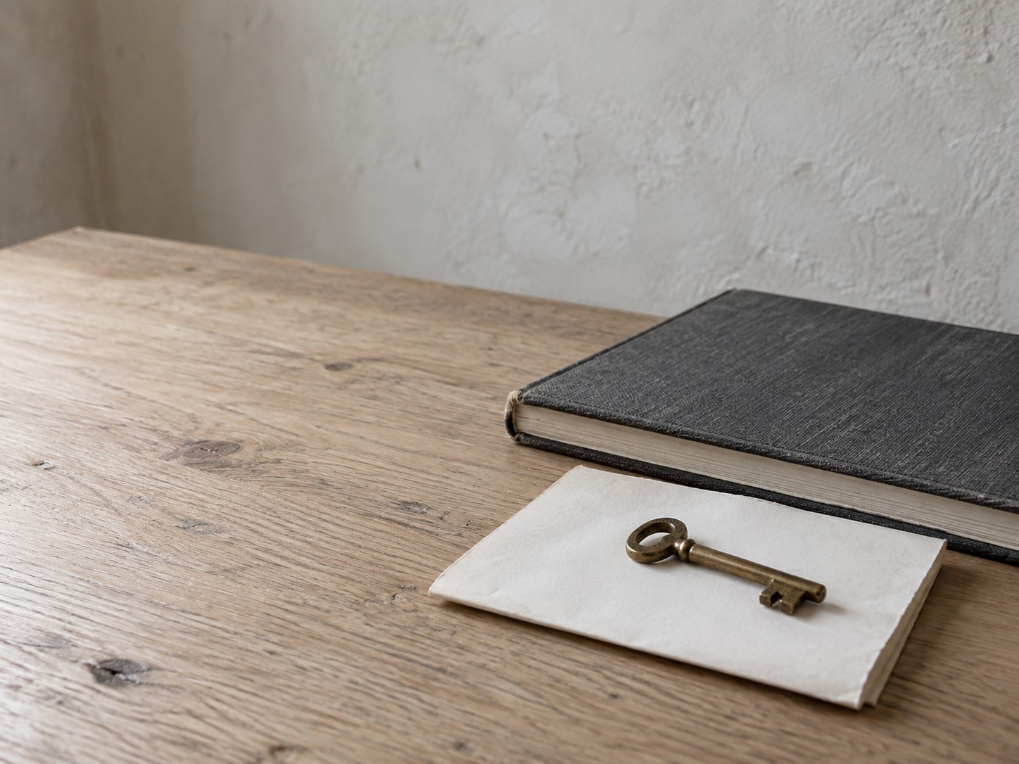 A small brass key resting on a folded blank sheet of paper beside a closed notebook on a light oak table.