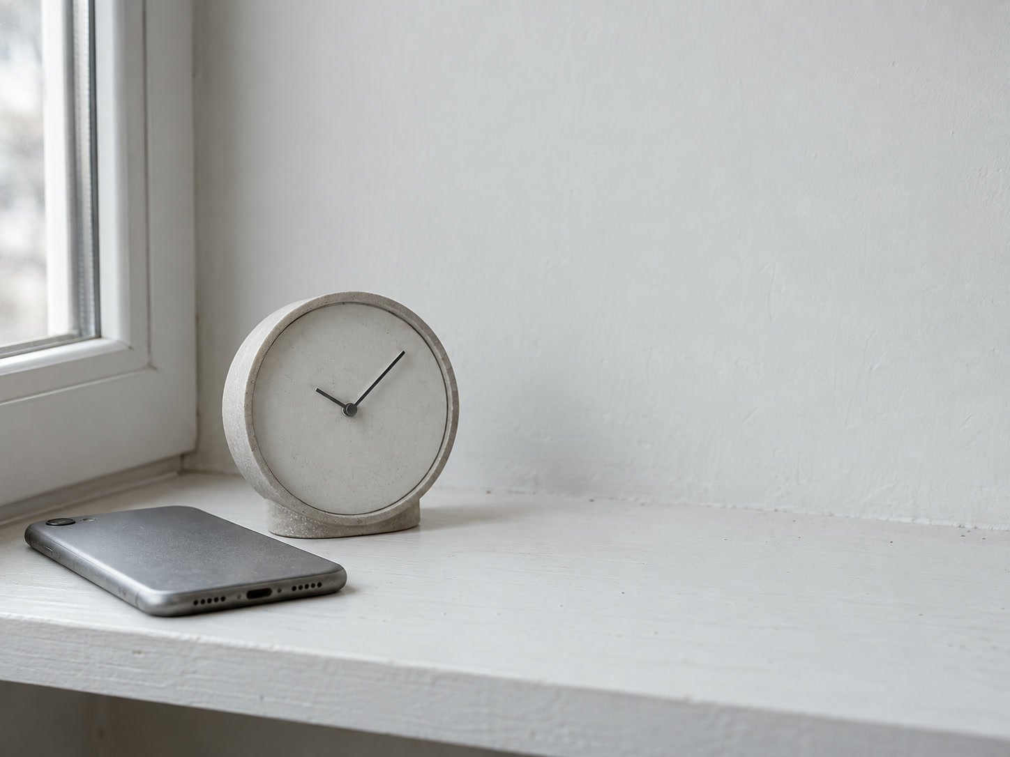 A small analog desk clock on a clean white shelf beside a phone lying face down.
