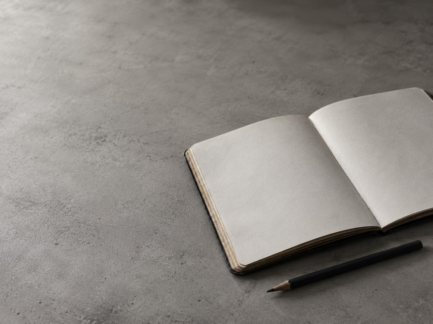 A worn notebook with blank pages open beside a pencil on a plain desk.