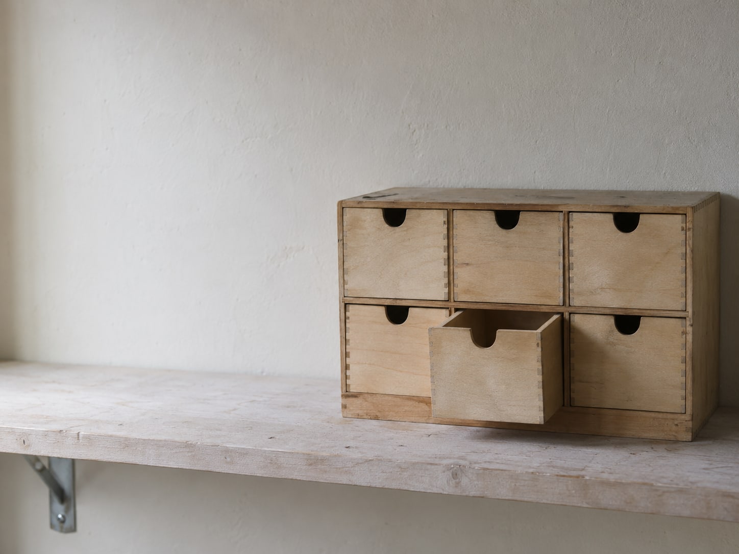 A tidy row of wooden drawers with blank fronts, one pulled open, on a plain workshop shelf.