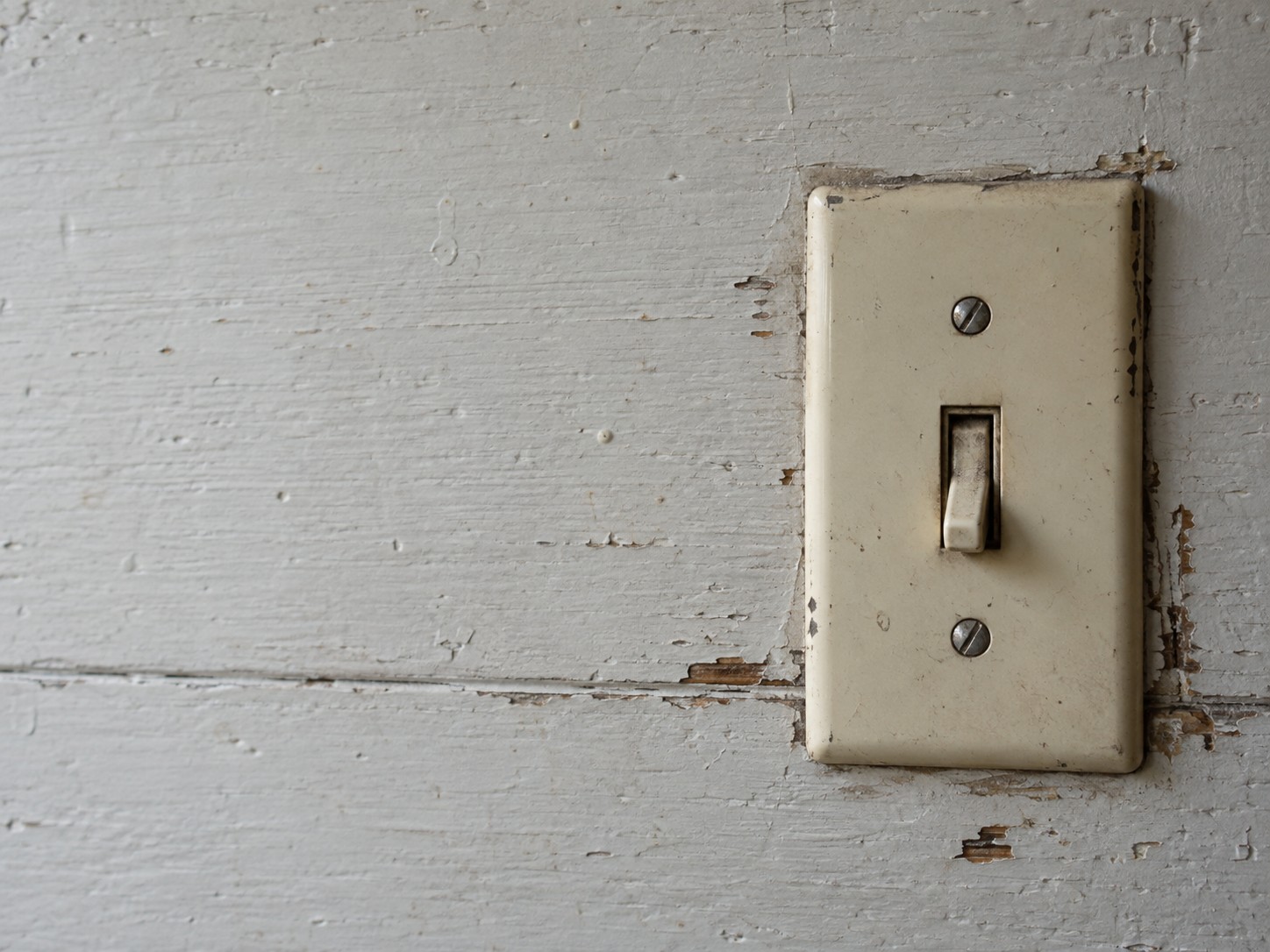 An old light switch plate in the off position mounted on a painted wooden board, lit from one side.