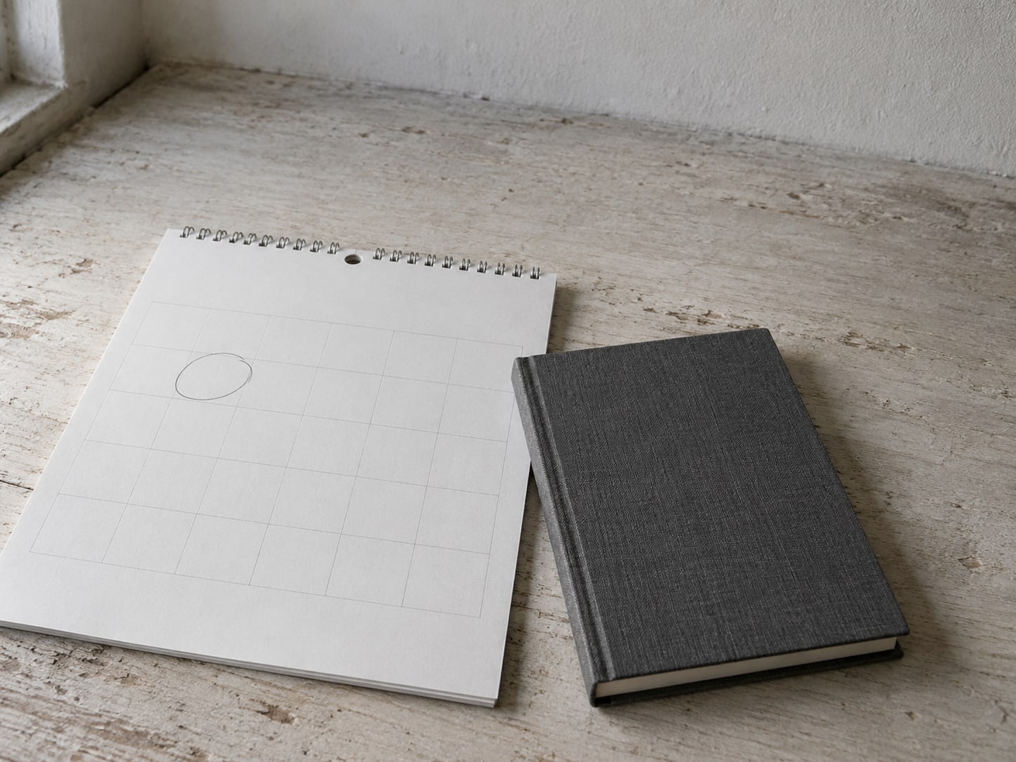 A paper wall calendar with one square circled in pencil beside a closed notebook.