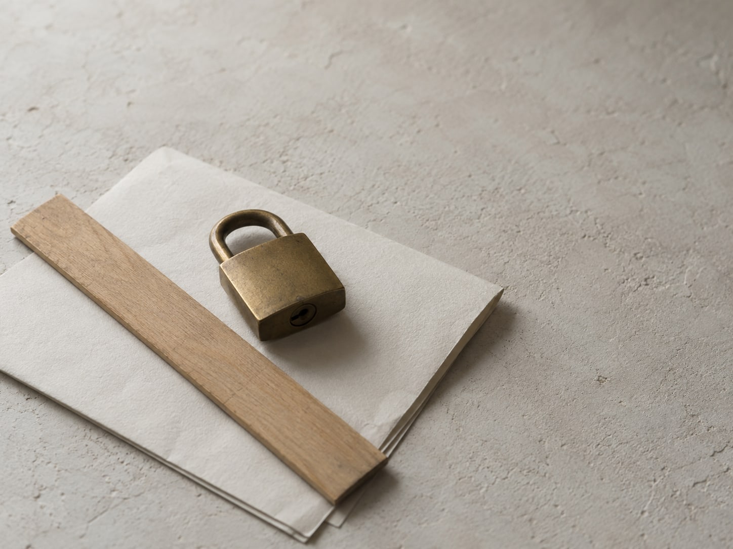 A small wooden ruler and a brass padlock resting on a folded sheet of blank paper.