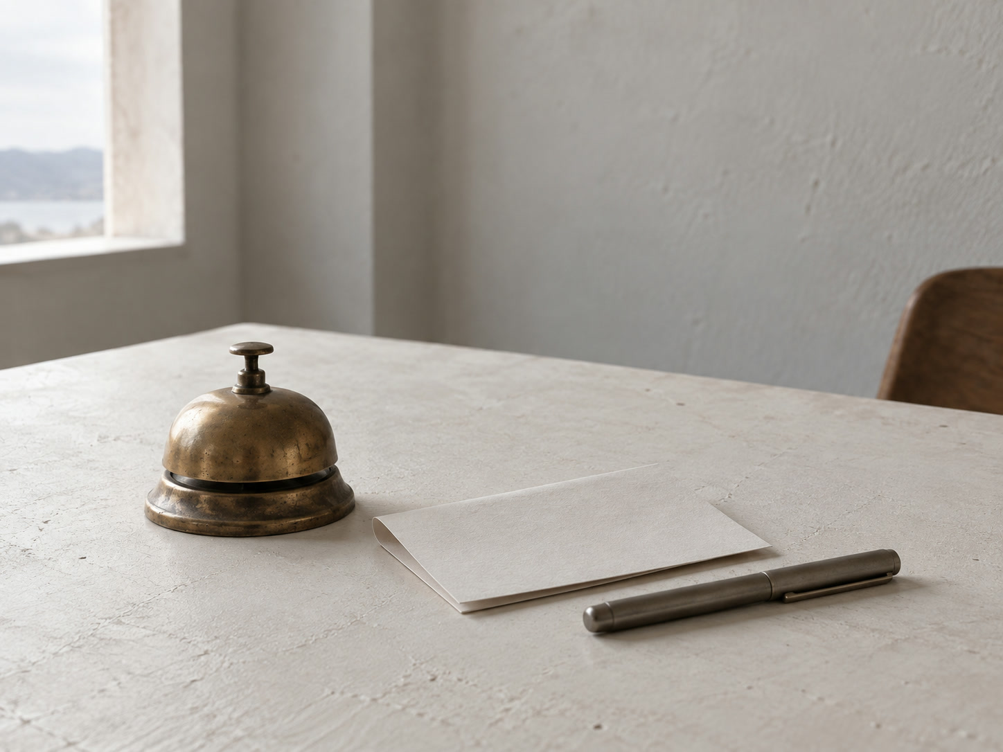 Una campana de escritorio de latón sobre una hoja de papel doblada en blanco y una pluma con capuchón sobre una mesa blanca.