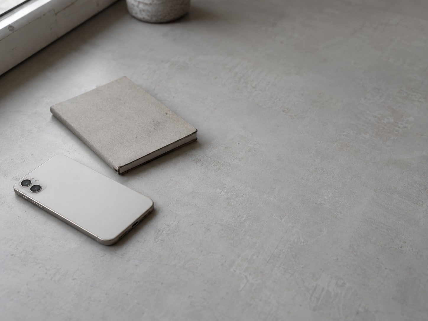 A pale smartphone lying face down on a desk beside a small notebook with faint pencil marks.