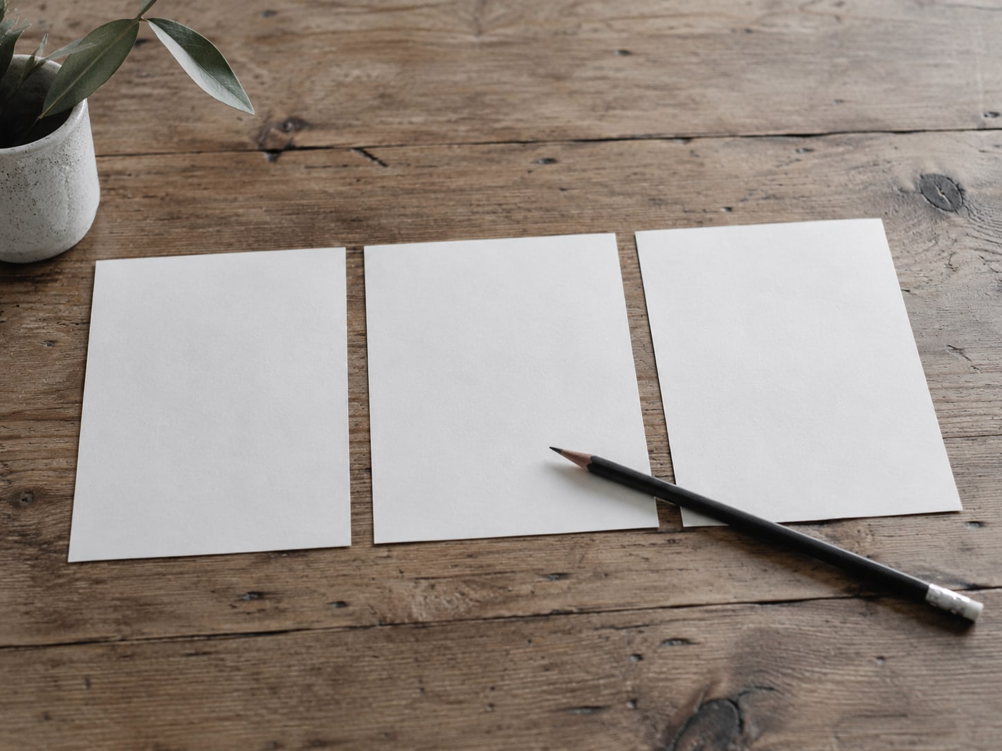 A tidy row of three blank paper checklists with a pencil laid across them on a wooden table.