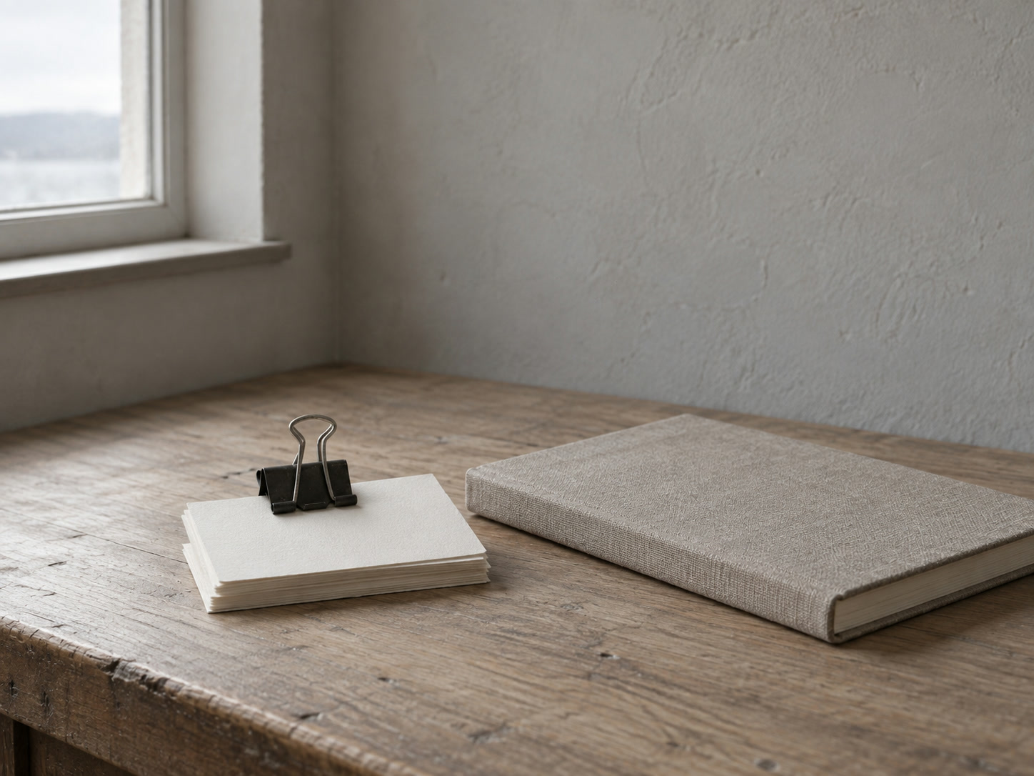 A small stack of blank index cards held with a binder clip beside a closed notebook on a desk.