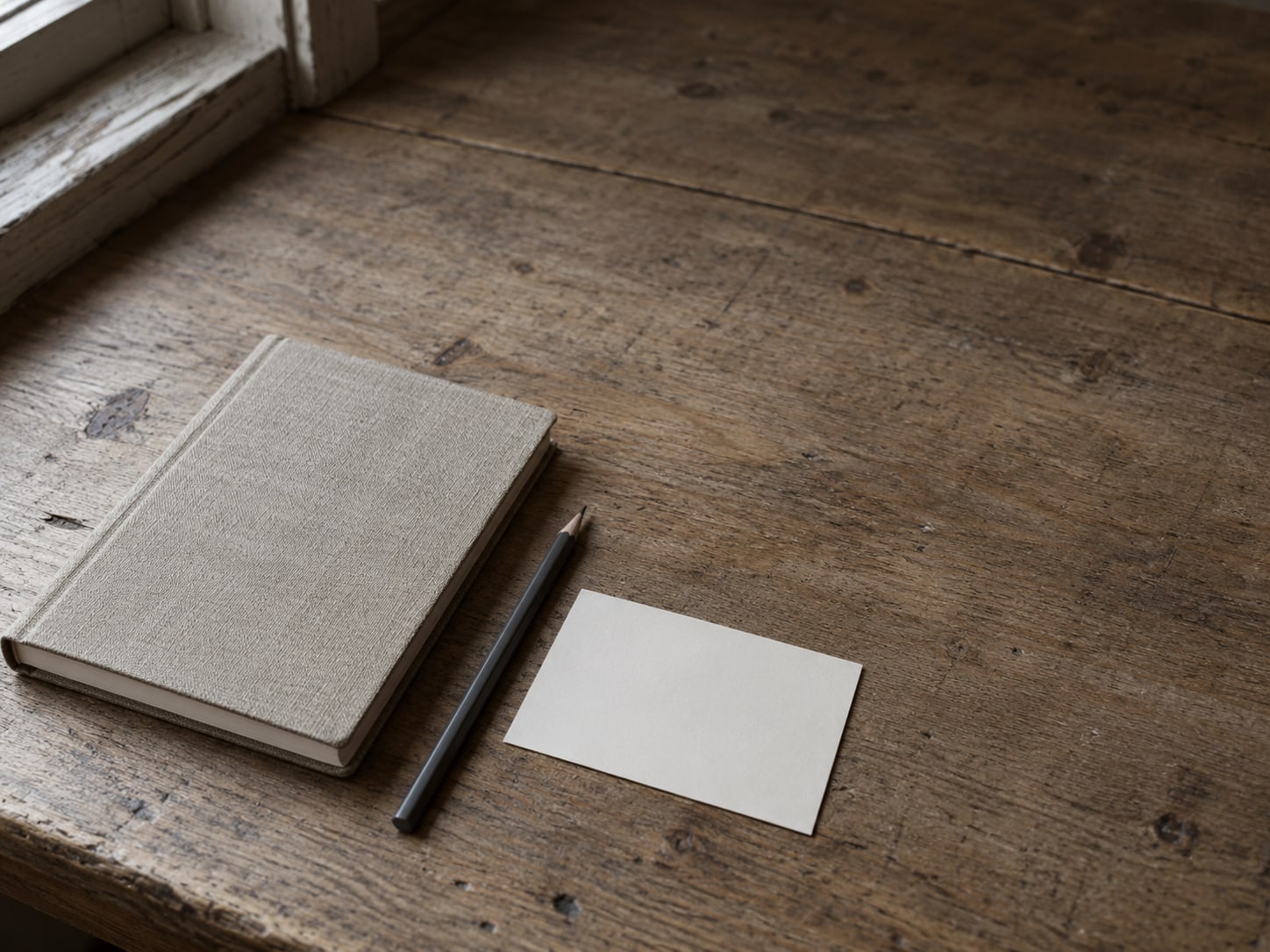 A closed notebook and a single pencil beside a blank appointment card on a worn desk.