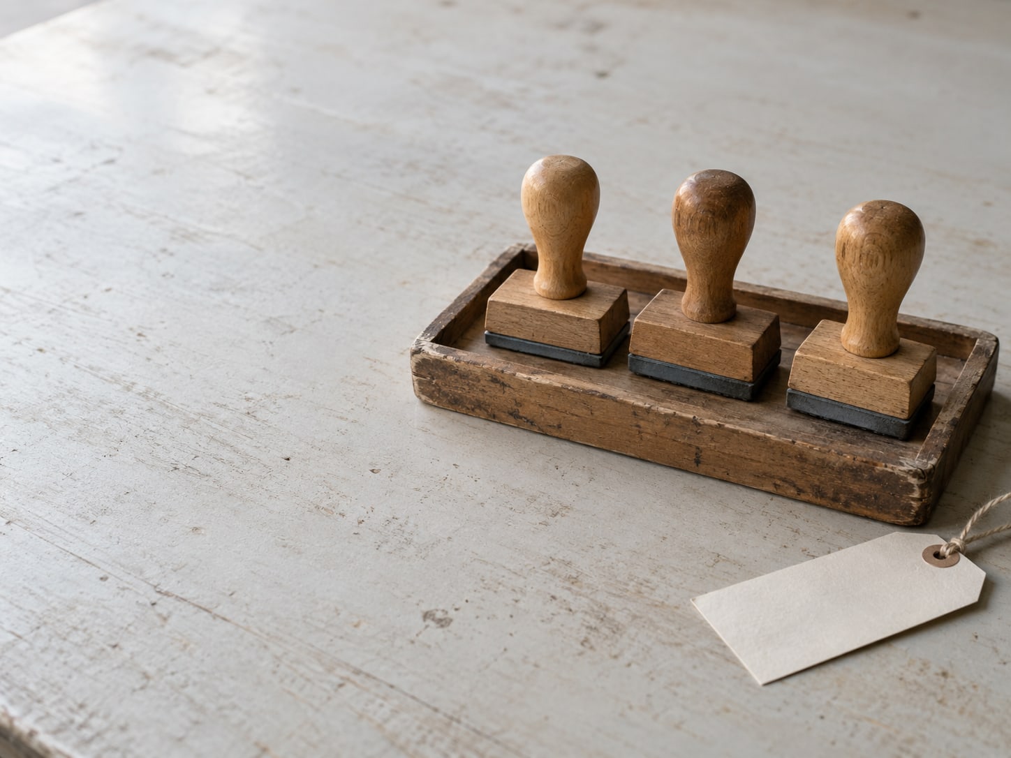 A tidy row of three rubber stamps on a wooden tray beside a blank paper tag.