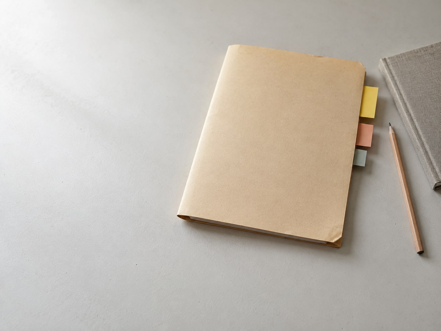 A manila folder with sticky tabs in three sizes sits beside a pencil and a closed notebook.