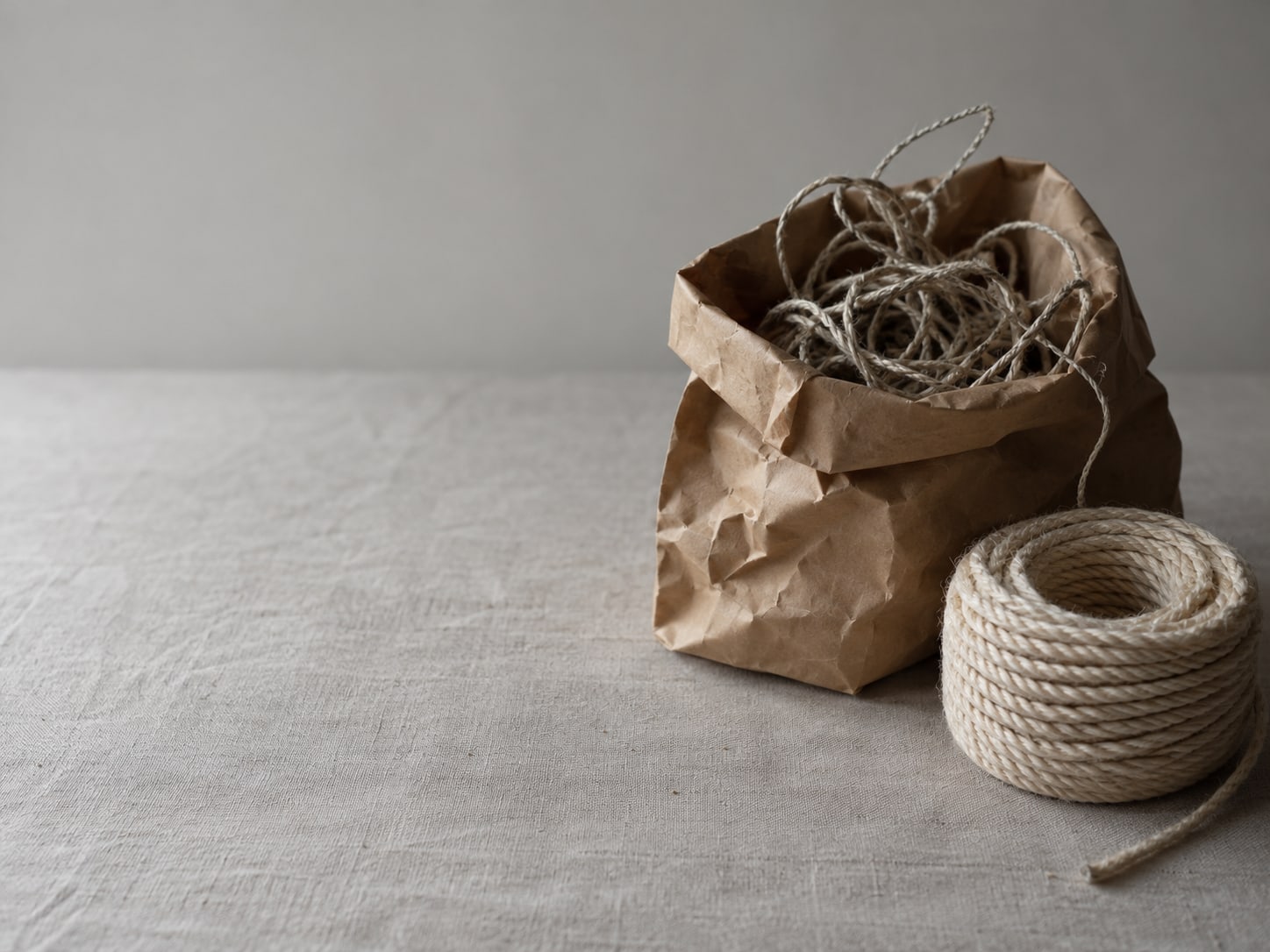 A paper bag of tangled string and a single neat coil of rope rest on a plain table.