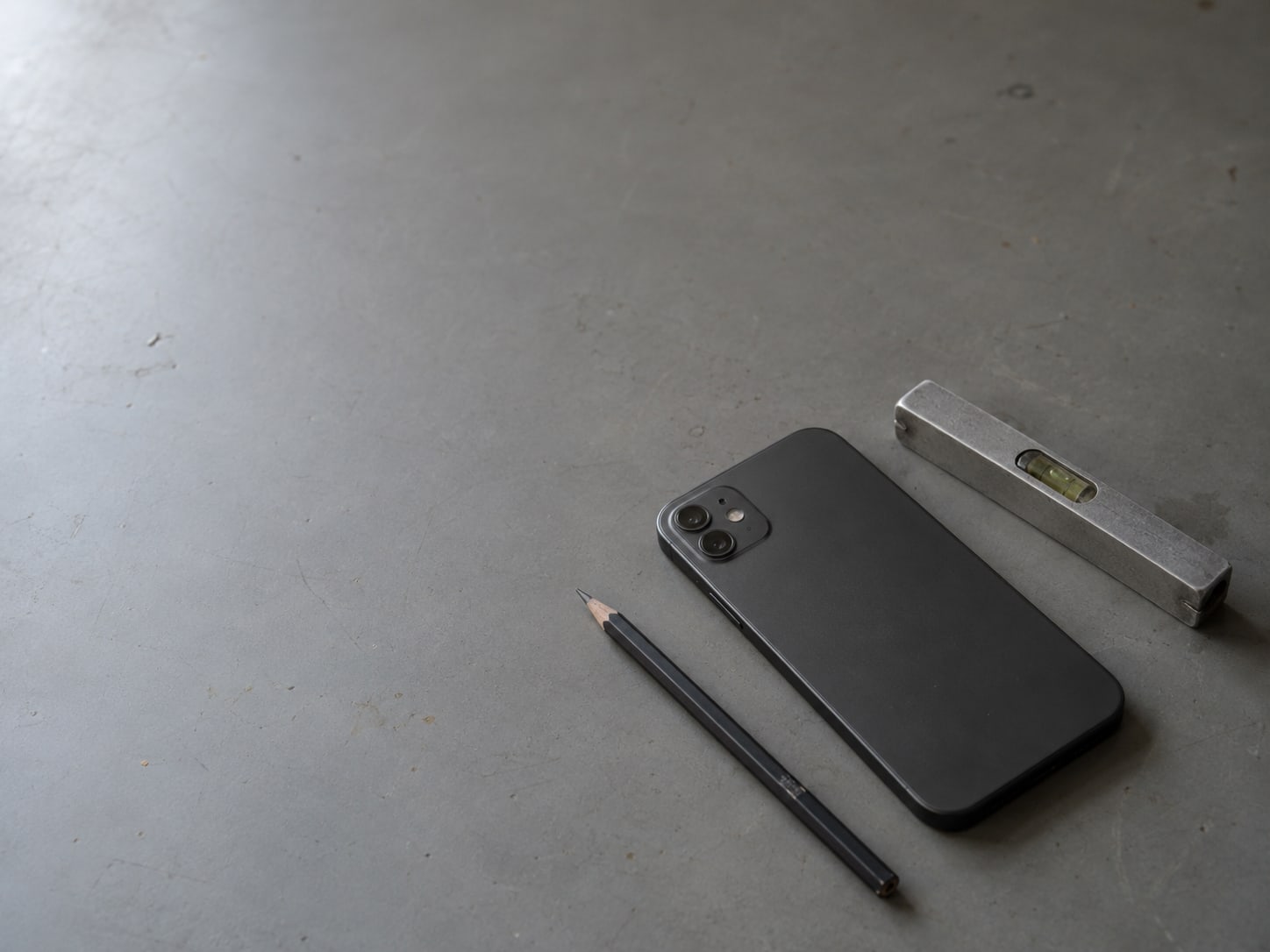 A smartphone lying face down on a desk beside a small level and a pencil.