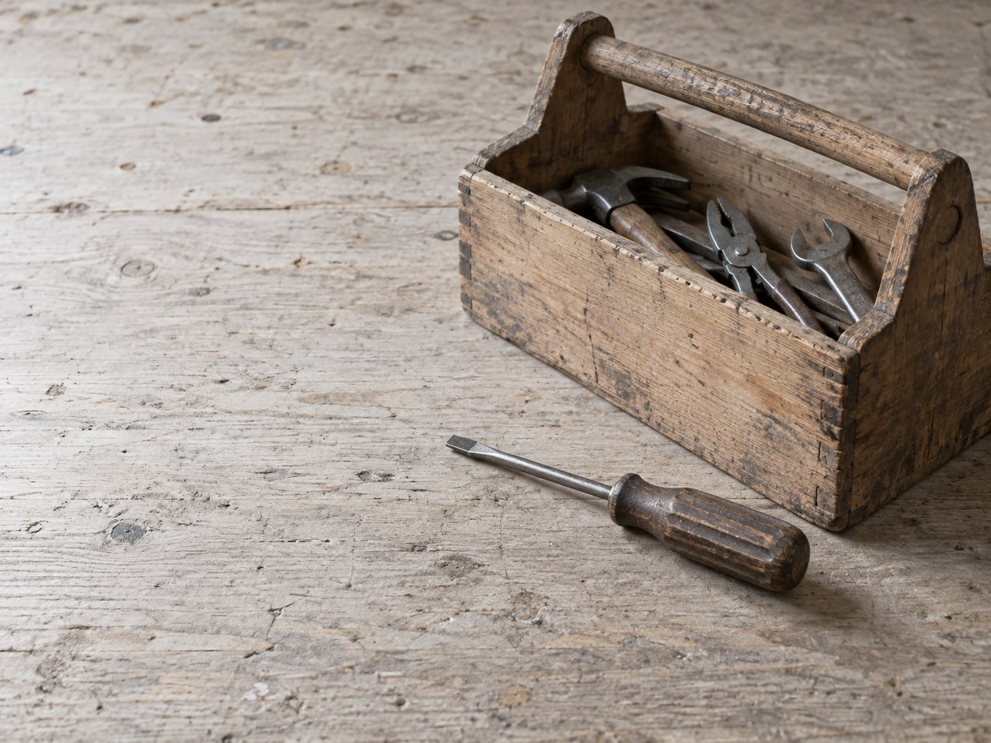 Una caja de herramientas de madera abierta sobre una mesa de trabajo con un solo desarmador colocado ordenadamente al lado y las demás herramientas aún dentro.
