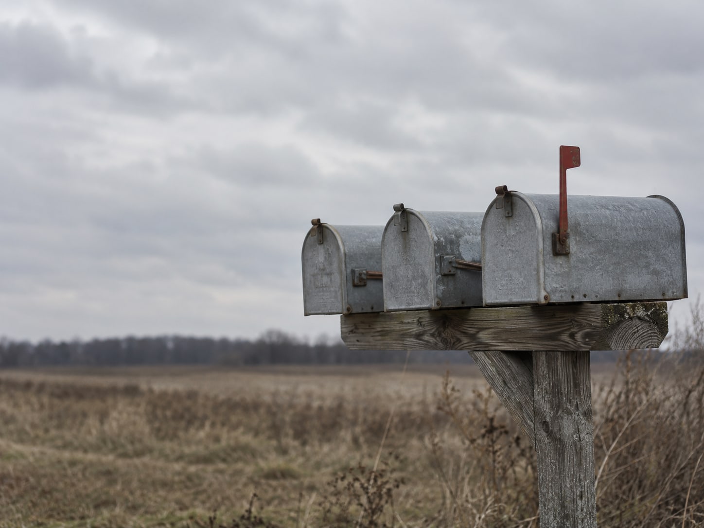 Three plain mailboxes on a wooden post, one with its small flag raised and the other two with flags down.