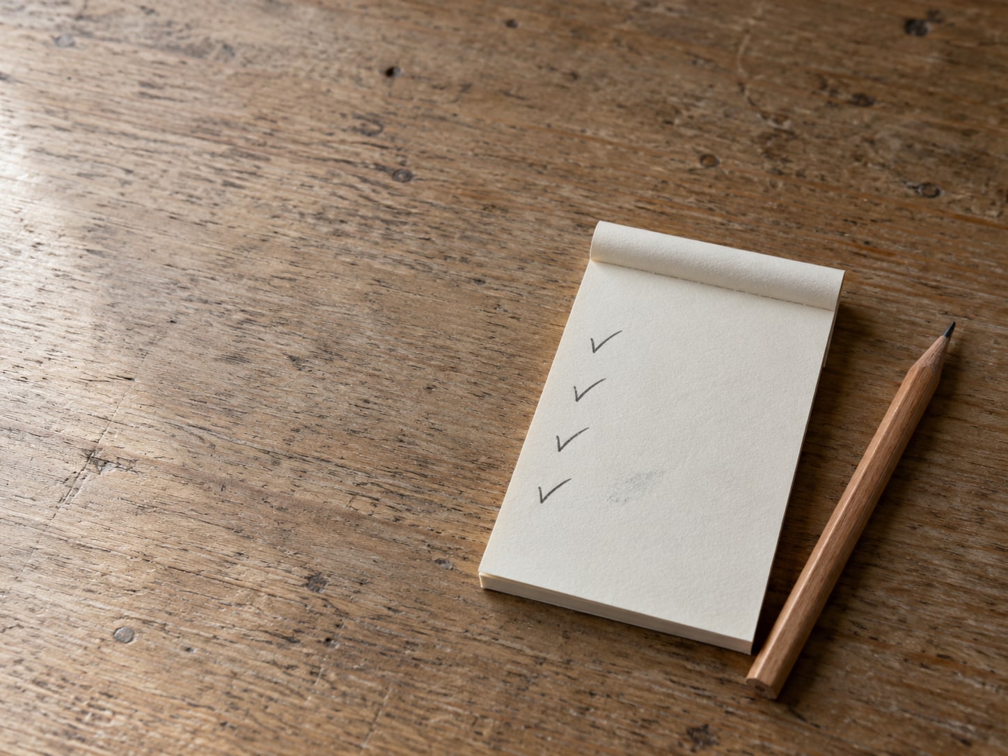A notepad with a short pencil-marked checklist and a single sharpened pencil resting on a tidy wooden desk.