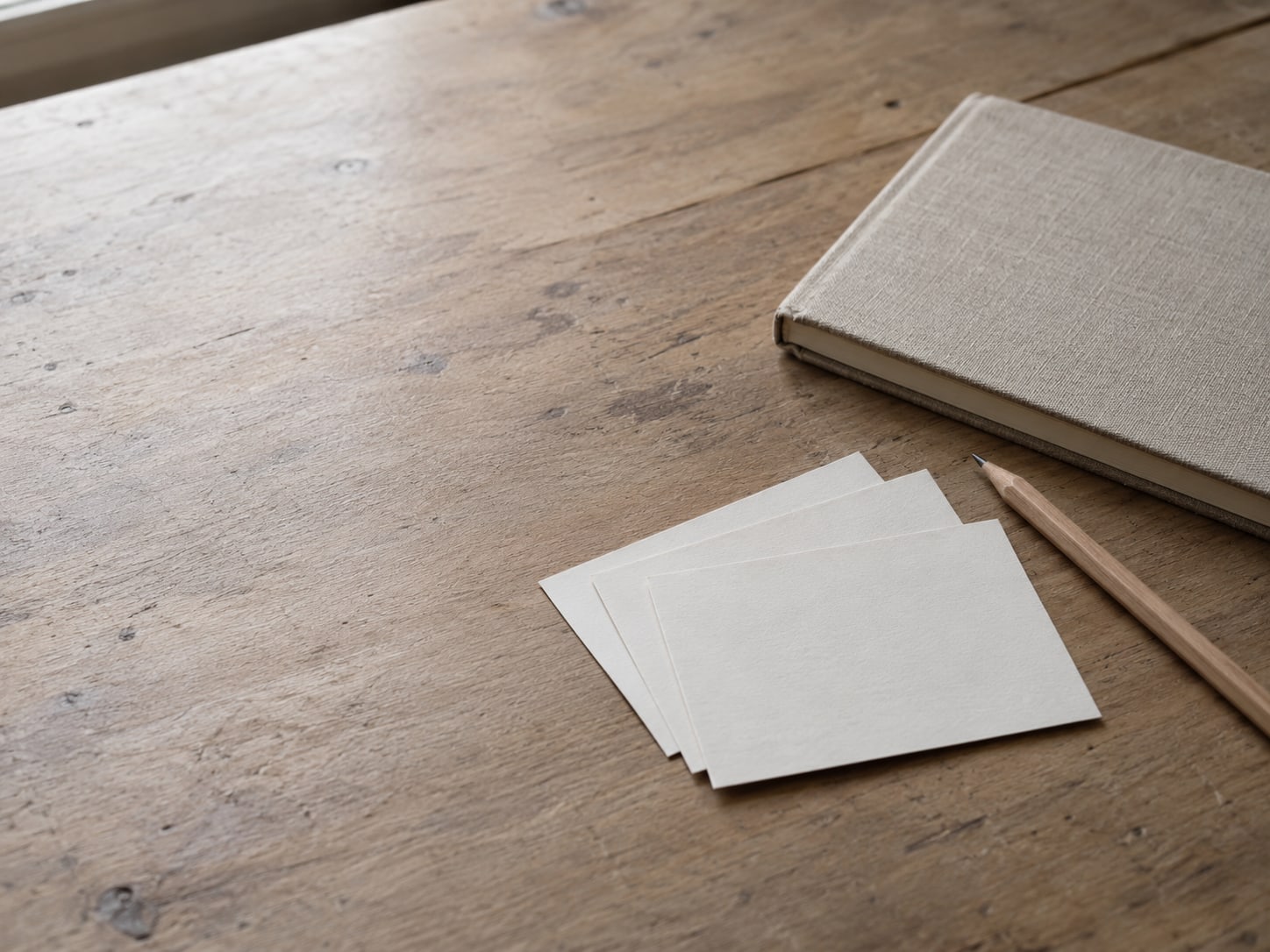 Three blank index cards fanned out on a wooden desk beside a closed notebook and a pencil.