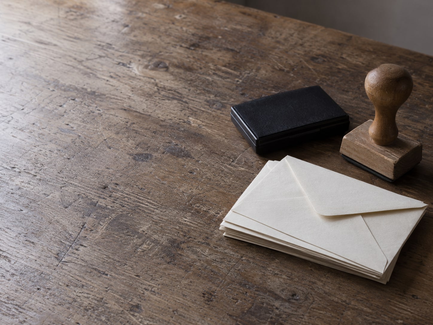 A rubber stamp and a closed ink pad beside a short stack of blank envelopes on a wooden table.