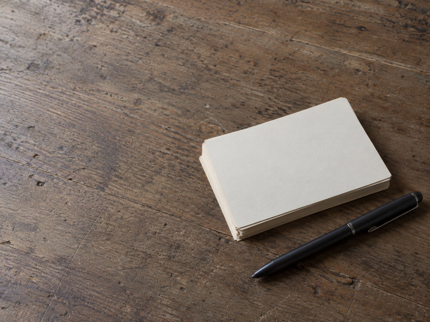 A small stack of blank cream cards and a pen resting on a wooden counter beside a closed address book.
