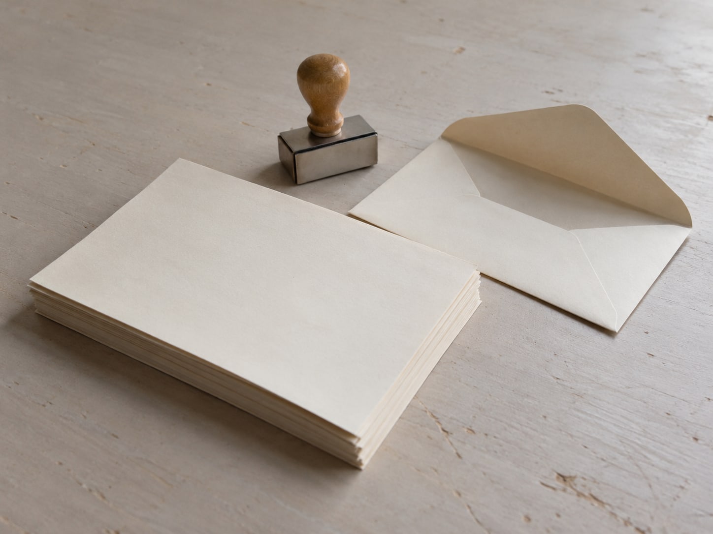 A stack of blank letters beside a small ink stamp and an open envelope on a plain desk.