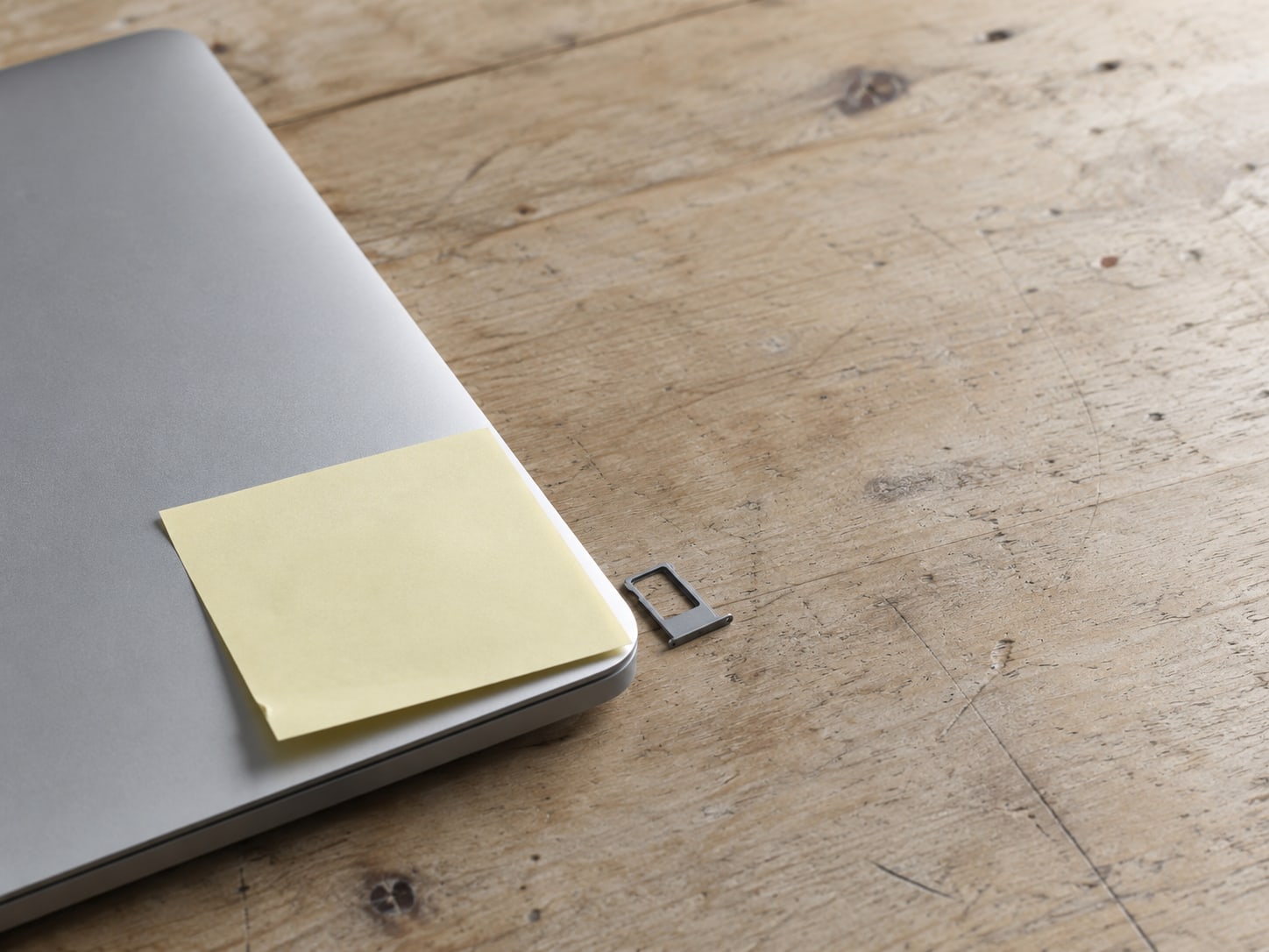 A blank sticky note pressed onto the edge of a closed laptop next to a spare SIM card tray.