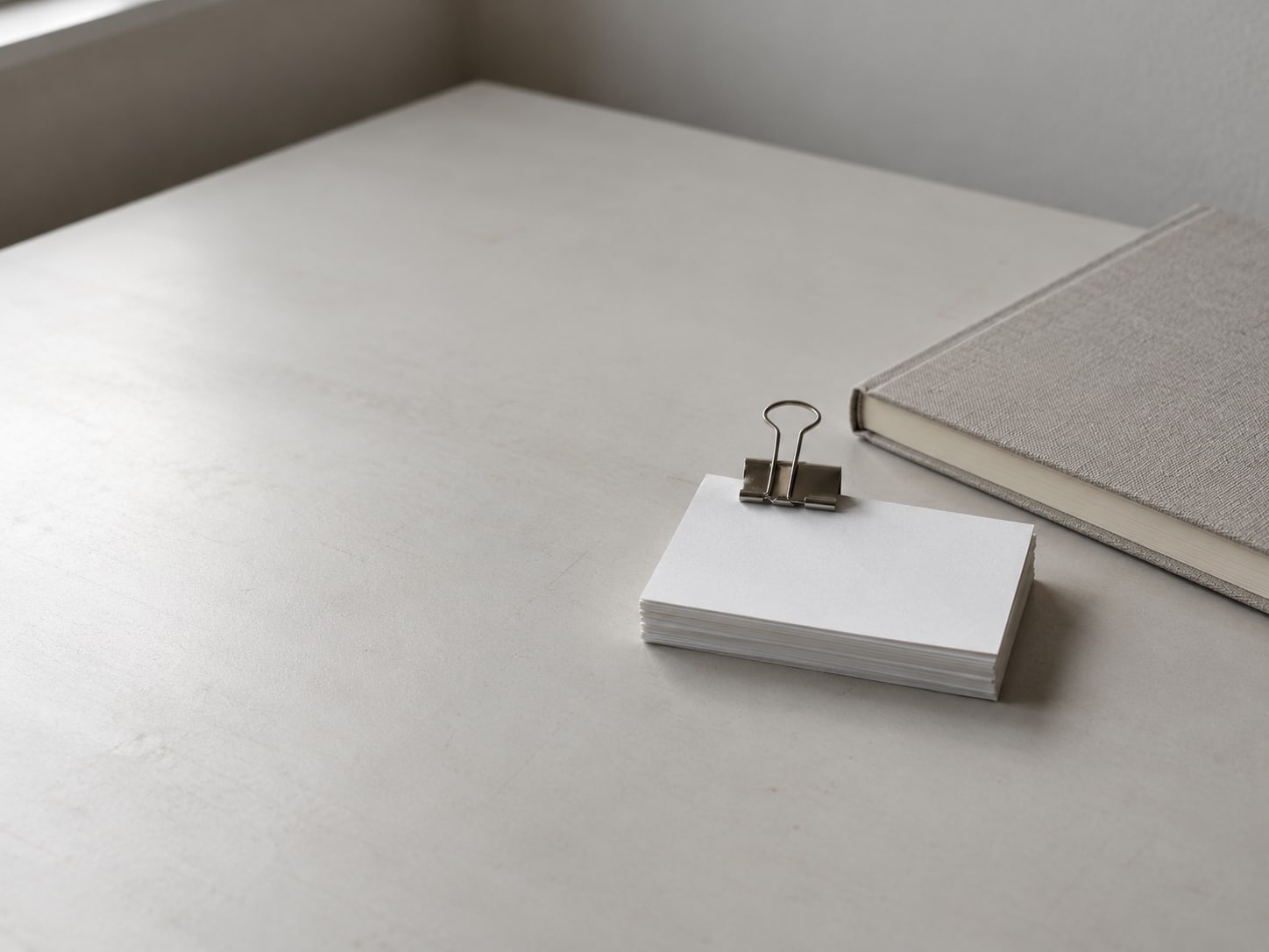 A small stack of index cards held together with a binder clip, resting beside a closed notebook on a tidy desk.