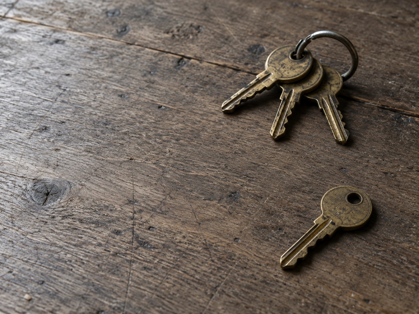 A single brass key lying apart from a ring of other keys on a wooden tabletop.