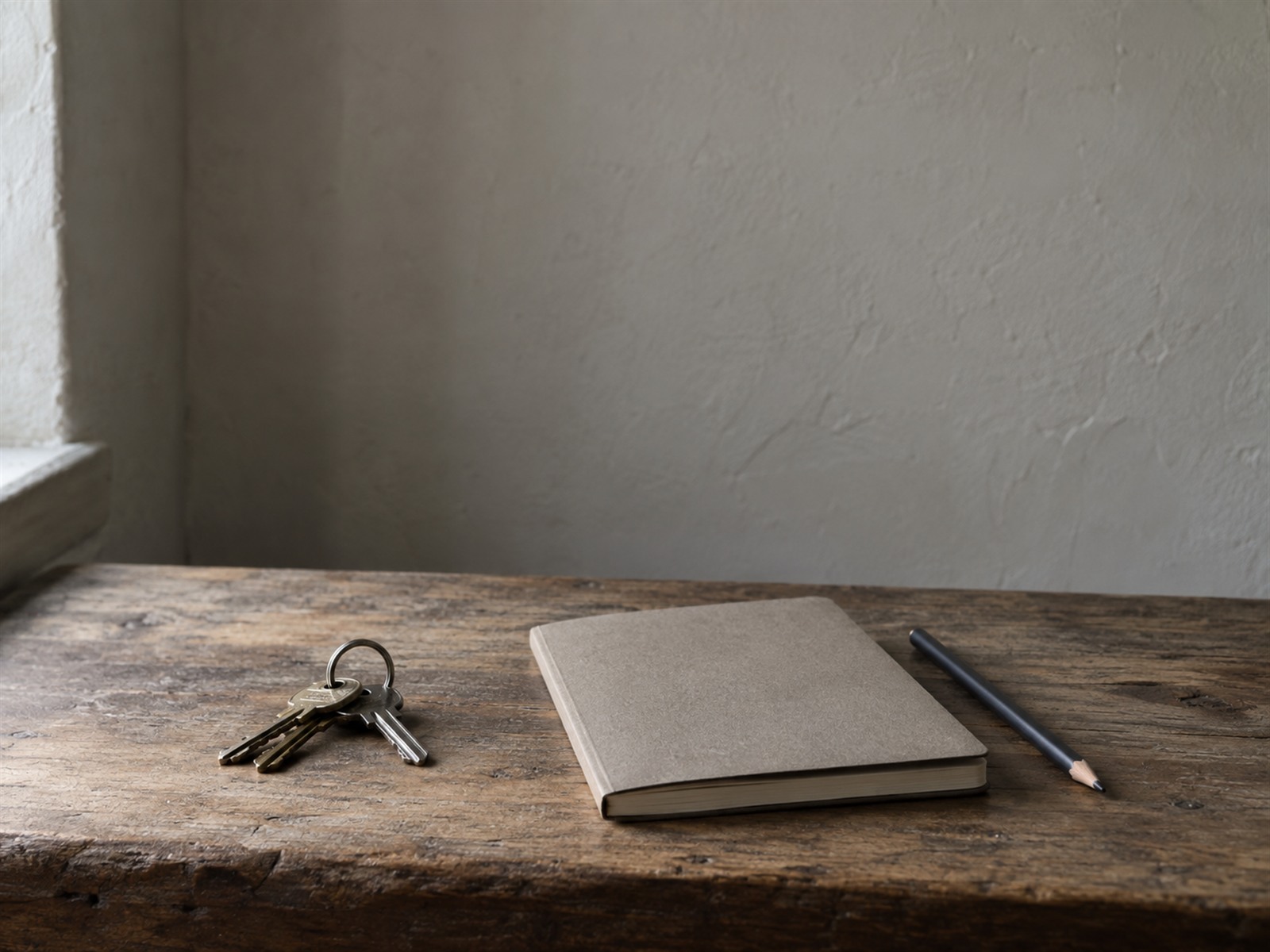 A ring of keys, a closed notebook and a pencil resting on a clean wooden counter in soft morning light.