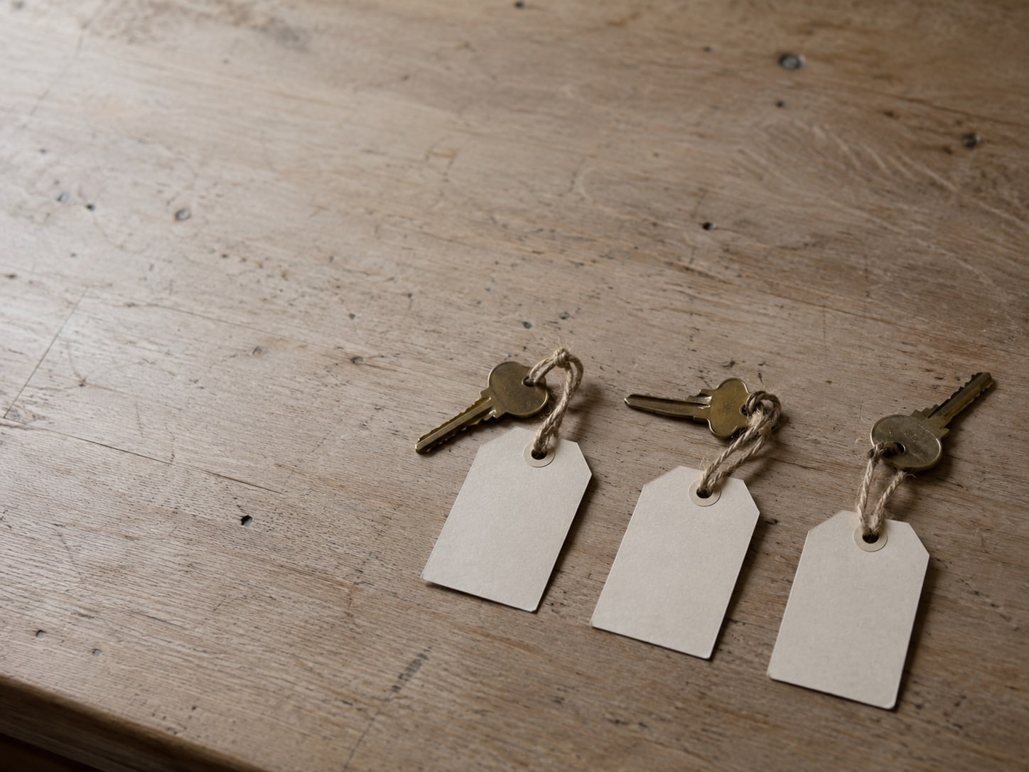 Three small blank tags tied to three brass keys laid in a row on a desk.