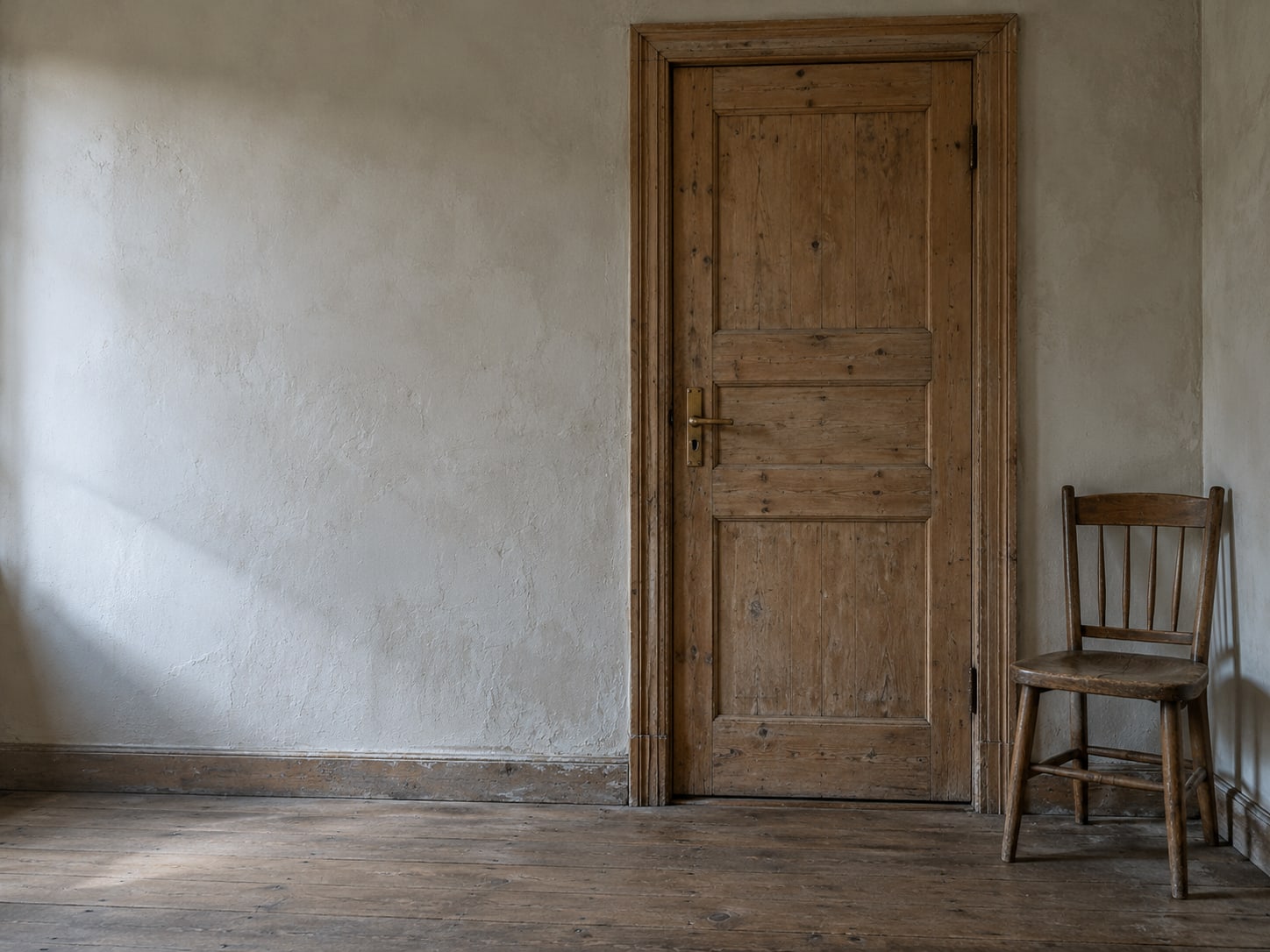 A closed wooden door with a brass handle beside an empty chair in a quiet hallway.