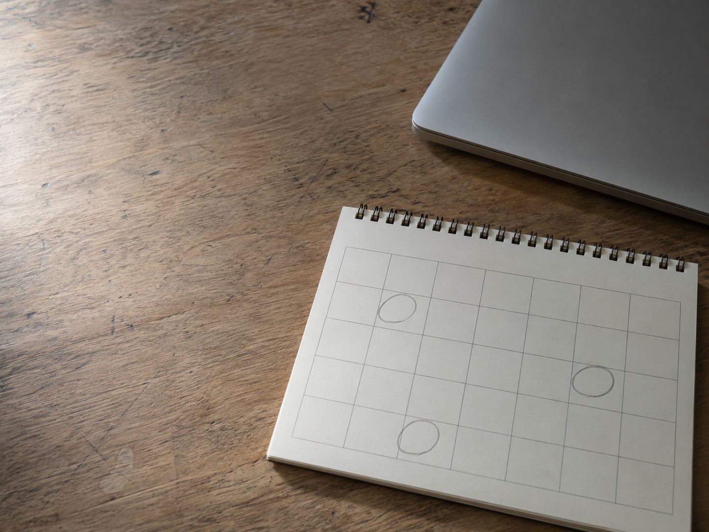 A desk calendar open to a month view with a few squares circled in pencil, next to a closed laptop.