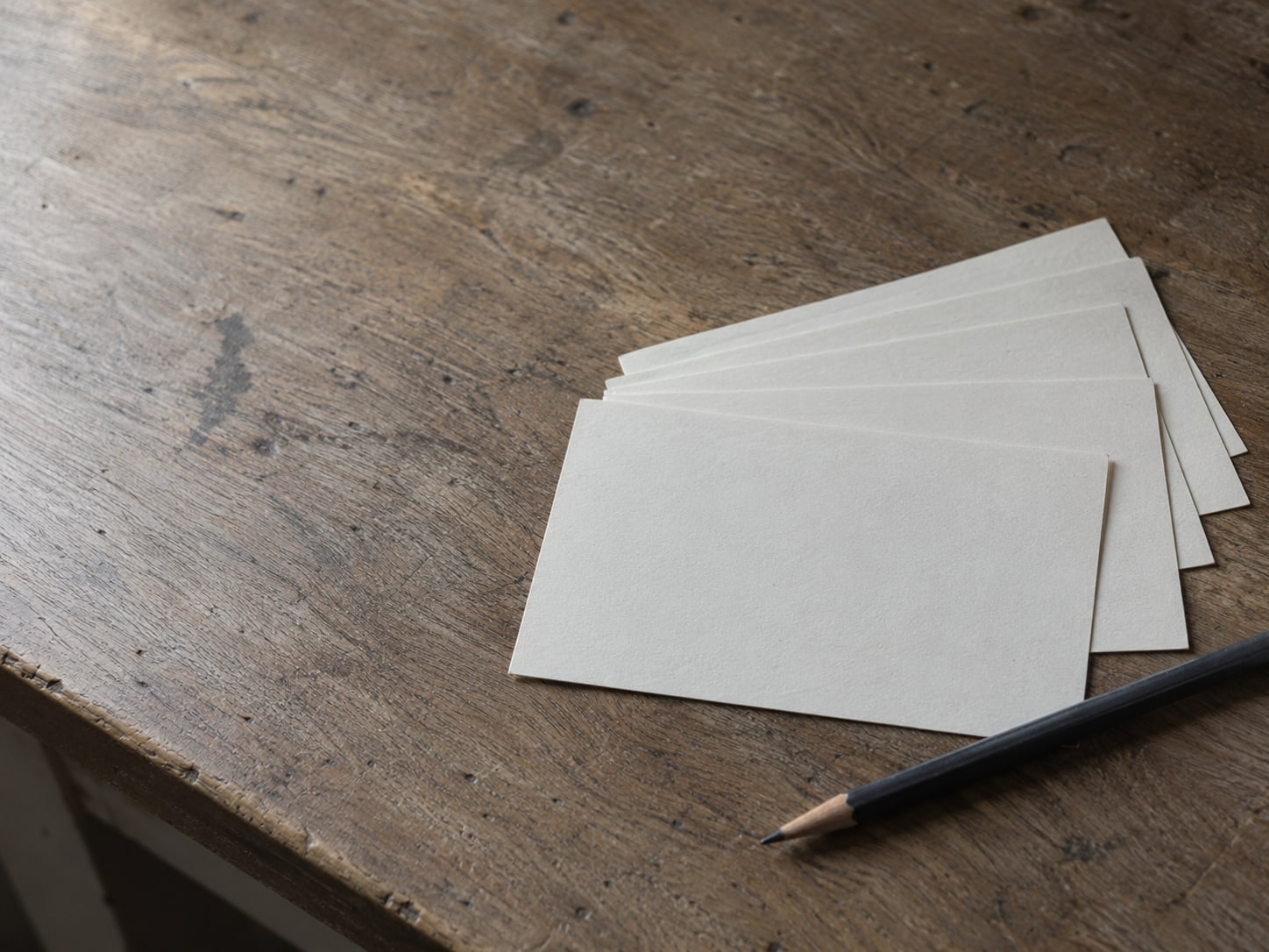 A row of blank index cards fanned out beside a pencil on a plain wooden desk.