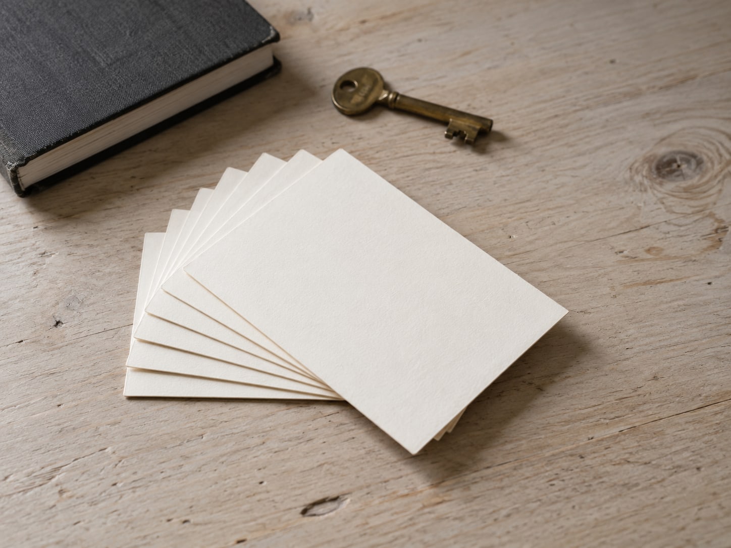 A closed notebook, a brass key and a small stack of index cards fanned out on a pale wooden desk.