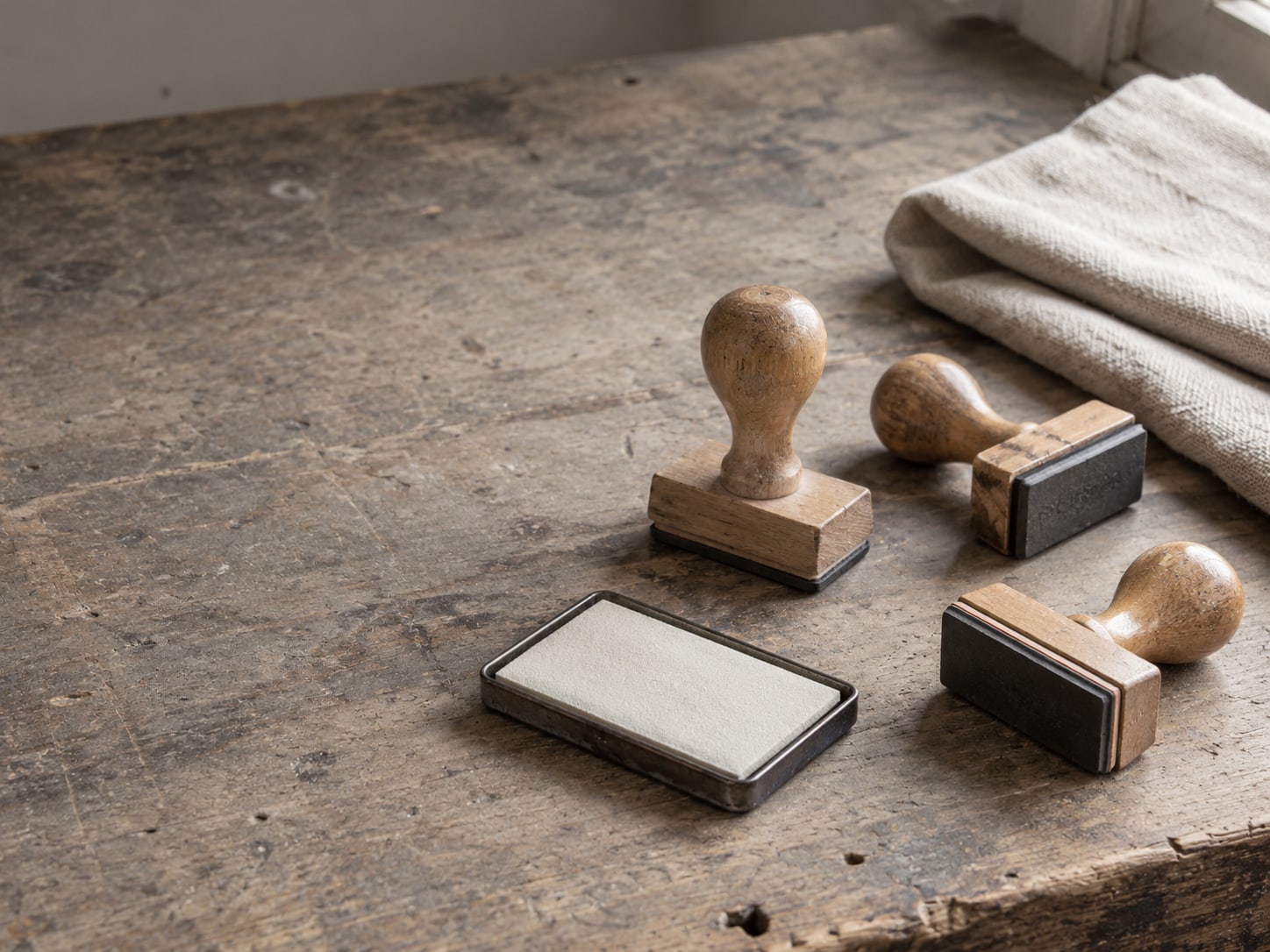 A set of blank rubber stamps and an inkless pad on a worn workshop bench beside a folded drop cloth.