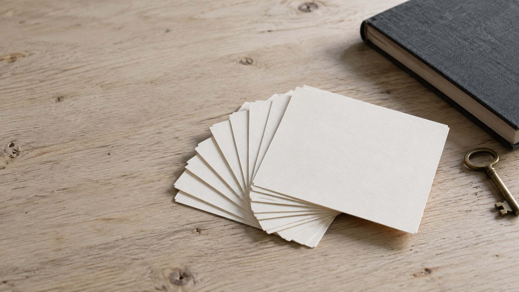 Un abanico de fichas en blanco extendidas sobre un escritorio de madera pálida, junto a una libreta cerrada y una llave de latón.