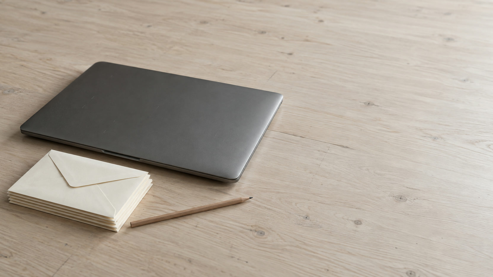 A small stack of sealed blank envelopes beside a closed laptop and a pencil on a pale desk.