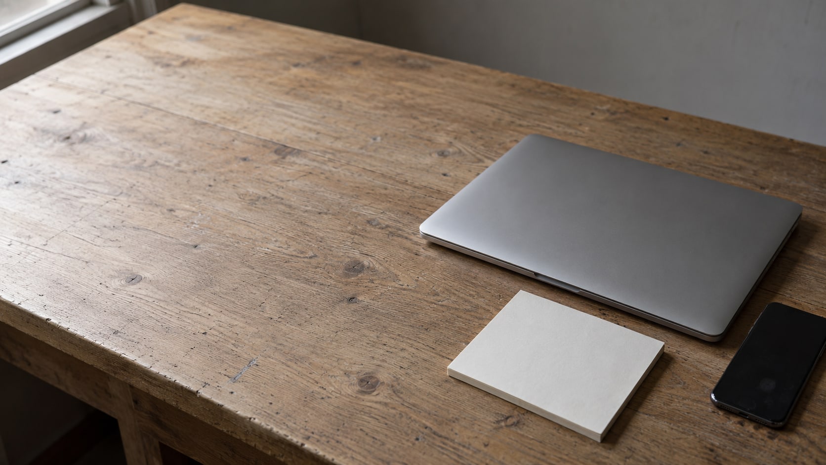 A closed laptop and a face-down phone on a quiet shop counter beside a blank paper pad.