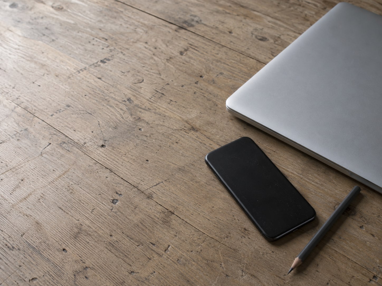 A smartphone lying face down beside a closed laptop and a plain pencil on a clean wooden desk.
